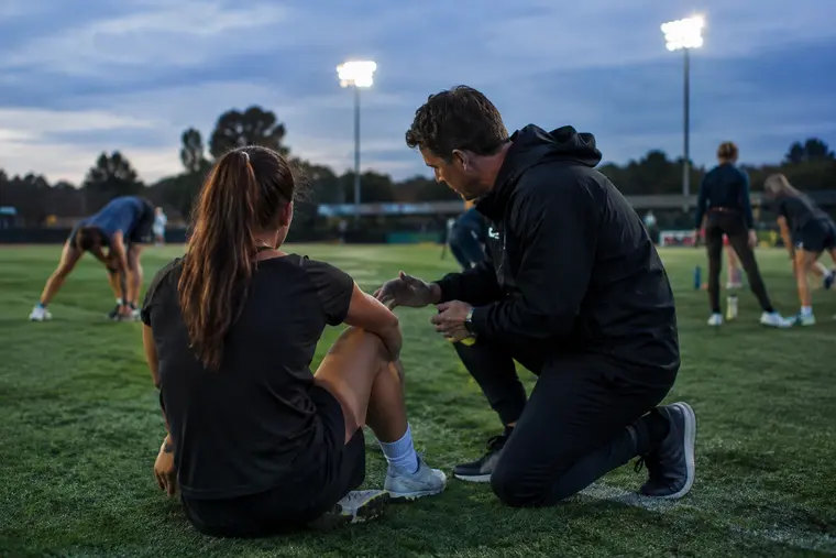 Football coach watches players run position drills during night practice
